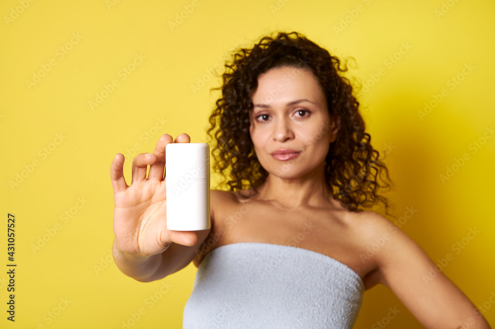 Soft focus on white container with cosmetic product in hand of beautiful half naked curly woman wrapped in bath towel Soft focus on white container with cosmetic product in hand of beautiful half naked curly woman wrapped in bath towel