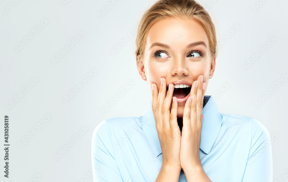 Woman happy and surprised shouts holds cheeks by hand .Beautiful girl in a blue shirt pointing to looking right . Presenting your product. Expressive facial expressions Woman happy and surprised shouts holds cheeks by hand .Beautiful girl in a blue shirt pointing to looking right . Presenting your product. Expressive facial expressions