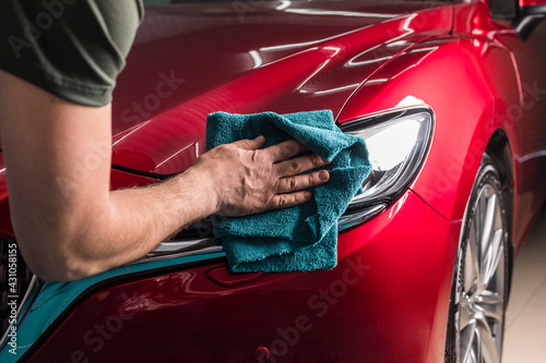 Car headlight polishing. A man cleans the headlight of a red car.
