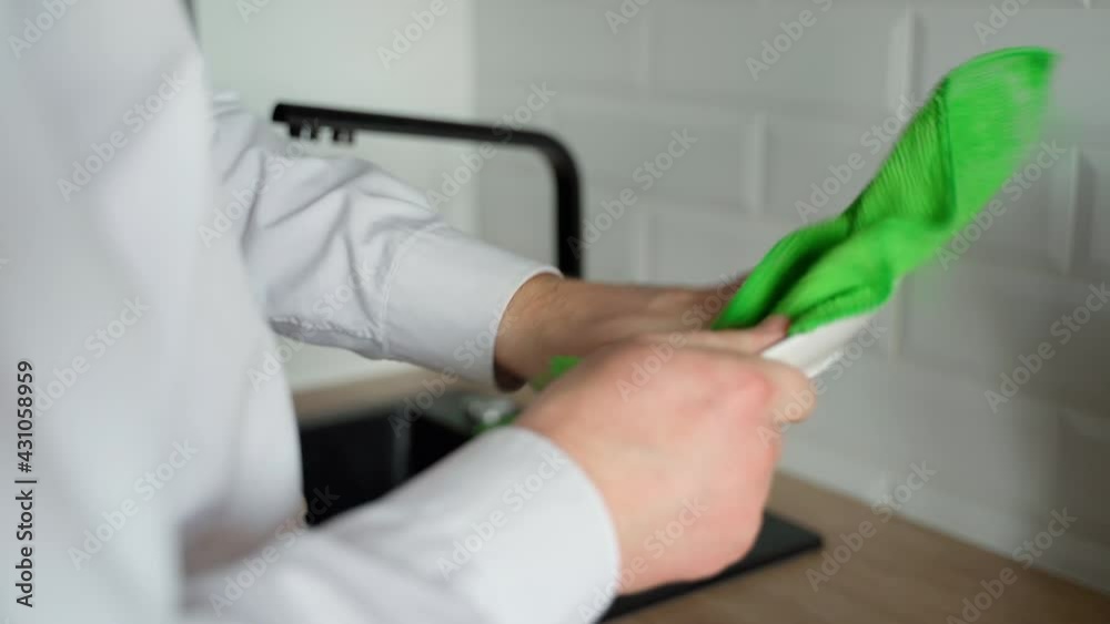 A man cleans a washed plate in a modern kitchen. You can see the towel, plate, hands and sink. Close-up A man cleans a washed plate in a modern kitchen. You can see the towel, plate, hands and sink. Close-up