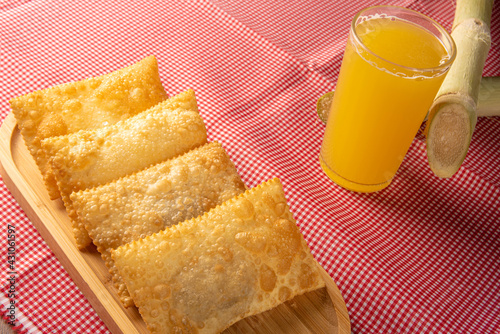 Brazilian fried pastries, a glass of sugarcane juice and canes positioned on a checkered tablecloth, black background, selective focus. photo