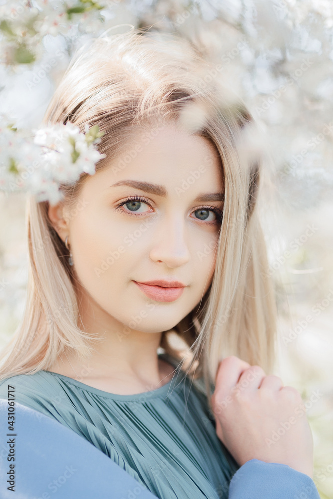 Vertical portrait attrective young beautiful blond woman in a flowering sakura garden
