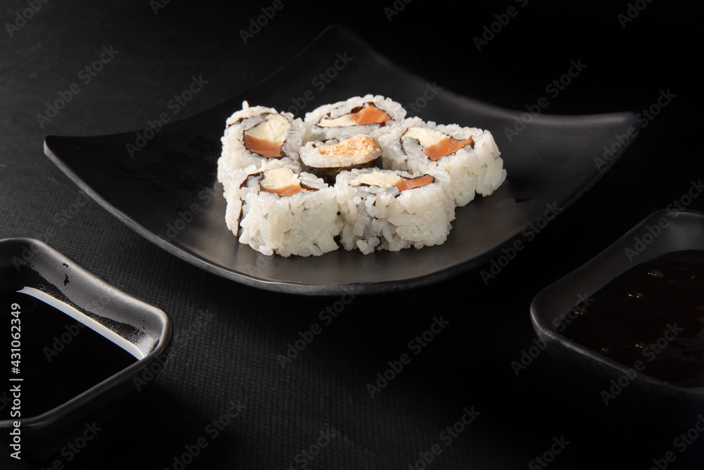 Sushi, beautiful sushi arrangement and shoyo sauce and tare made in black dishes on a dark surface, black background, selective focus. Sushi, beautiful sushi arrangement and shoyo sauce and tare made in black dishes on a dark surface, black background, selective focus.