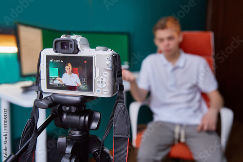 An influential person who creates content for social networks. A teenager takes a video in front of a camera in his room next to a computer monitor