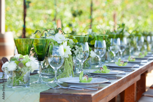 Long wood table and chairs in vineyard set for party with flowers, glassware, wine glasses, plates and silverware 