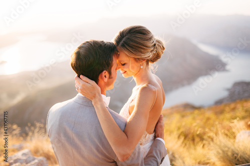 The bride and groom sitting on the top of Mount Lovcen overlooking the Bay of Kotor, smiling and hugging tenderly, close-up 