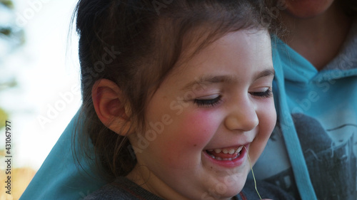 Dark hair and rosy cheeks girl laughing with mother browsing serfing network with mobilephone during sunset on camping vacation. Concept of nature quality family time. Extremly close up
