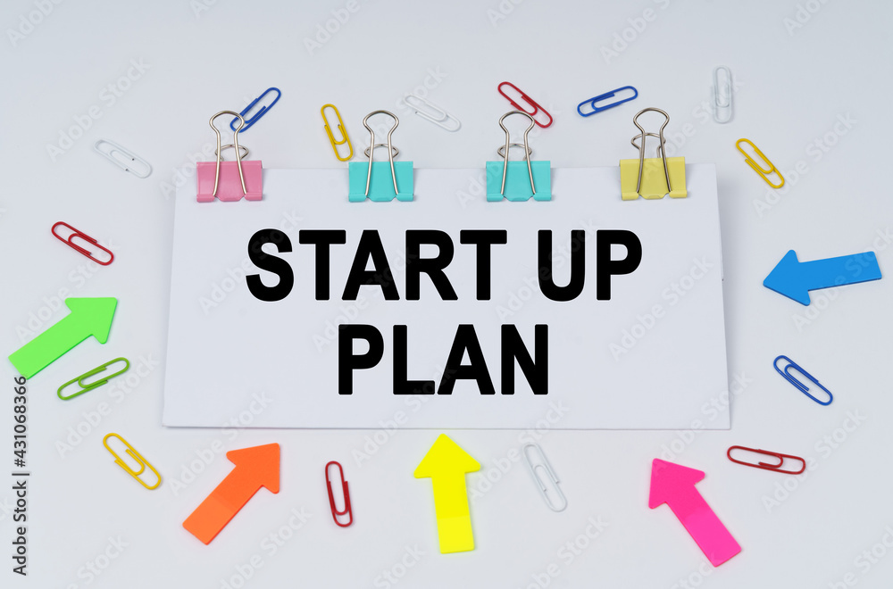On the table there are paper clips and directional arrows, a sign that says - Start Up Plan On the table there are paper clips and directional arrows, a sign that says - Start Up Plan