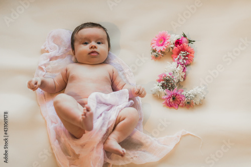 Newborn baby. Lying on the bed. Naked. Flowers. On a light background.