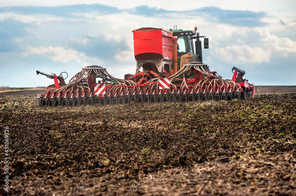 Fototapeta premium Farmers sow, using tractor with seeder in a plowed field, apply fertilizer, sowing time