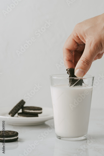 A cookie held by a female hand while inside a glass of milk