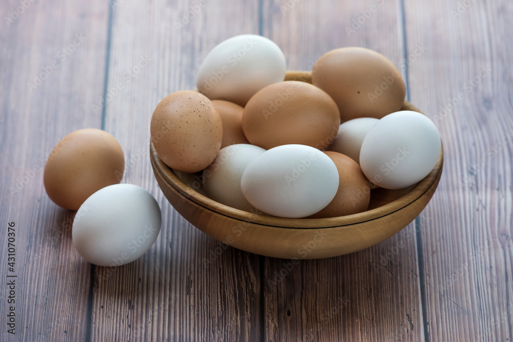 Wooden bowl with brown and white chicken eggs on wood table. Brown and white eggs in bowl on wood background. Free-range organic eggs. Healthy food concept Wooden bowl with brown and white chicken eggs on wood table. Brown and white eggs in bowl on wood background. Free-range organic eggs. Healthy food concept