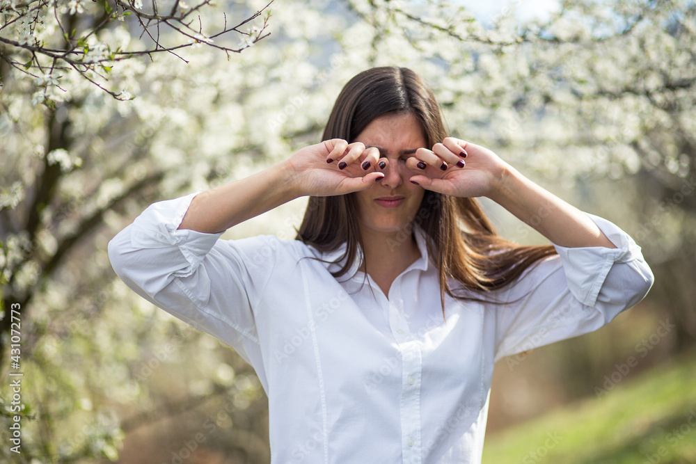 Woman suffering from strong eye pain against spring trees