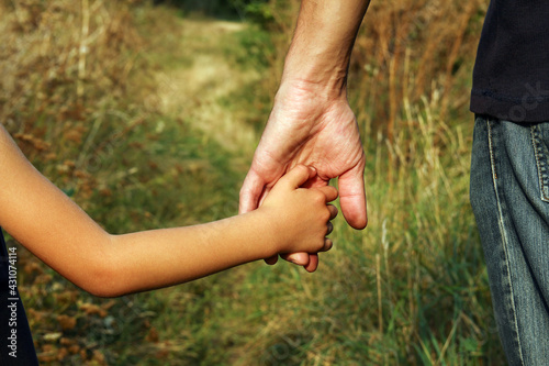 the parent holds the hand of a small child in a park
