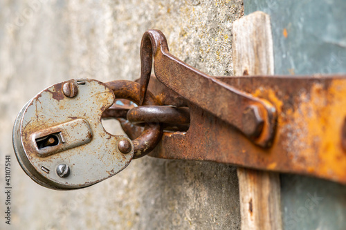 The padlock is hanging on the door. A large barn lock on a rusty door hinge.