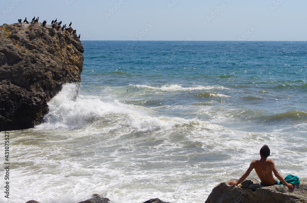 Young tanned boy admiring the sea storm waves