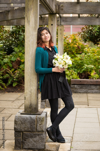 Biracial young teen bridesmaid holding flower bouquet outdoors under pergola