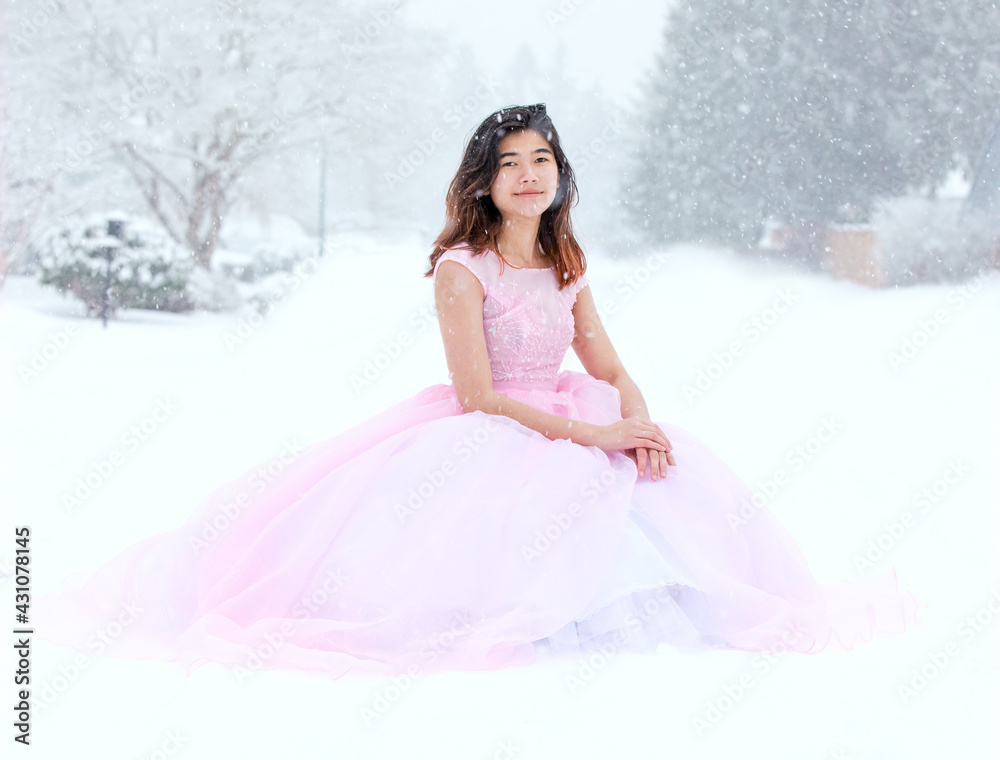 Teen girl in pink formal gown sitting outdoors in snow Teen girl in pink formal gown sitting outdoors in snow