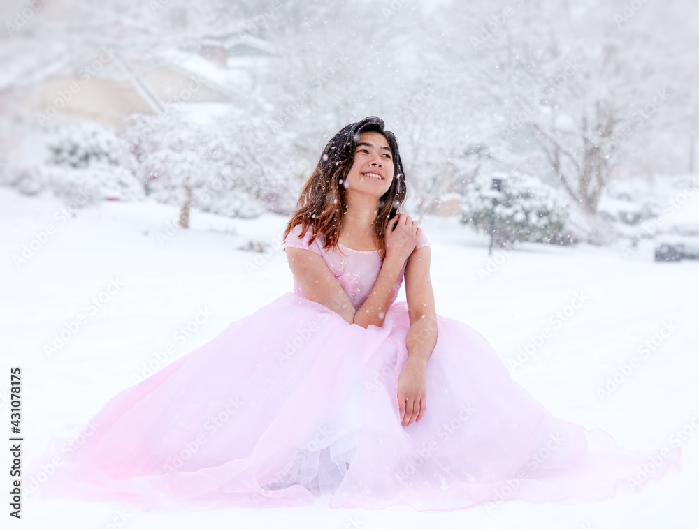 Teen girl in pink formal gown sitting outdoors in snow Teen girl in pink formal gown sitting outdoors in snow