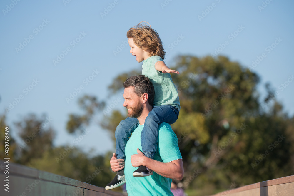 Daddy piggyback his little son outside. Handsome father piggybacking son playing on nature, dad holding riding on back adorable cheerful kid boy enjoy active game.