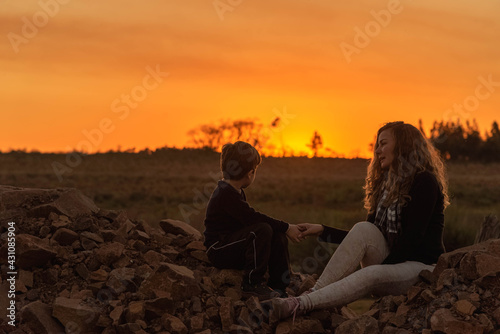 Mother and son sitting on rocks contemplating nature at sunset time.