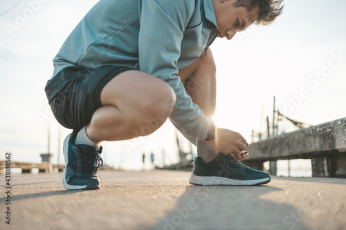 closeup of man tying shoe laces on the road before running in sunset. Sport and workout concept.