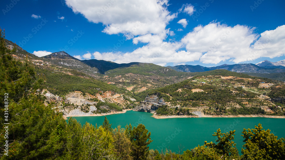 Panoramic view of a mountain lake with clear turquoise-green water against the background of a road and a village of farmers