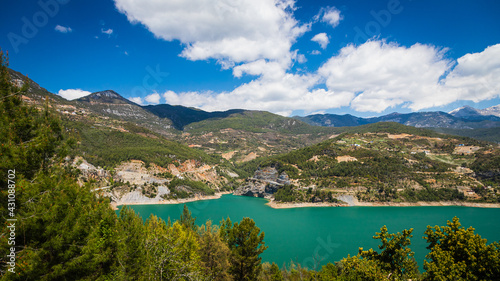 Panoramic view of a mountain lake with clear turquoise-green water against the background of a road and a village of farmers