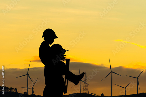 Silhouette of father and son with clipping path in hard hat, Happy dad carrying son on shoulders checking project at wind farm site on sunset in evening time