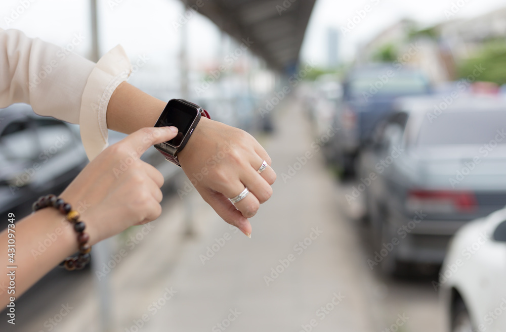Woman touch a smart watch on her left hand on background car park