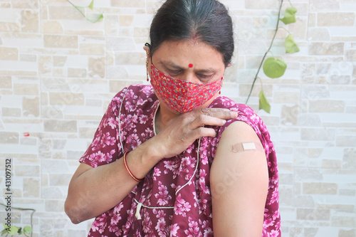 Фотография Indian woman looking at bandage applied after getting vaccination during new strain of covid-19, Mature Woman wearing mask received a coronavirus vaccine on her arm