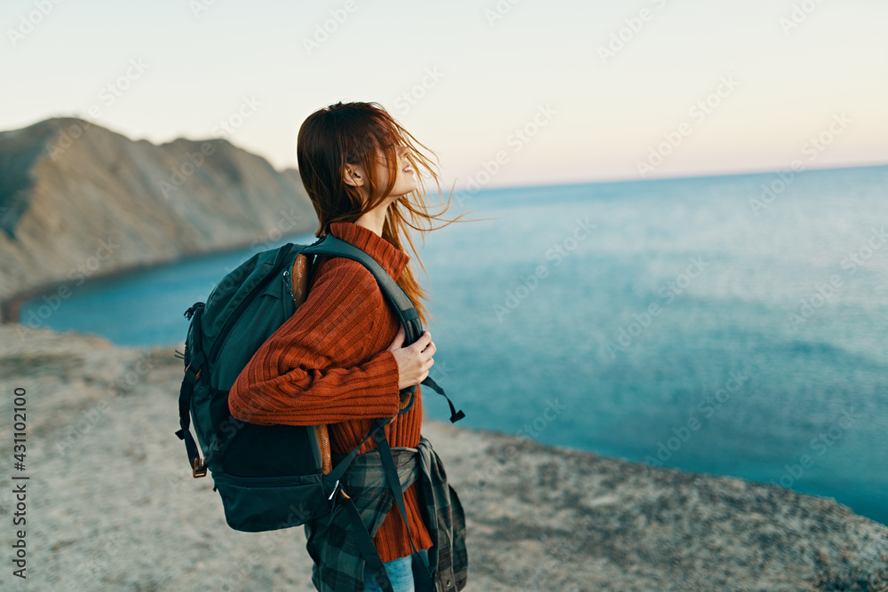 happy traveler in a red sweater with a backpack on her back look at the sea in the distance and high mountains