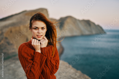 happy woman in a red sweater in the mountains in nature and the sea in the background