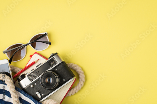 Above photo of sunglasses phone bag camera notebook and pencil isolated on the yellow background with empty space