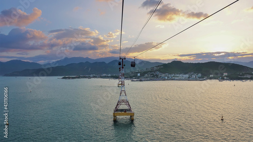 The cable car runs across the bay. High supports rise above the water. Town houses on the shore. A mountain range against the backdrop of a sunset sky with rose-gold clouds. Nha Trang. Vietnam