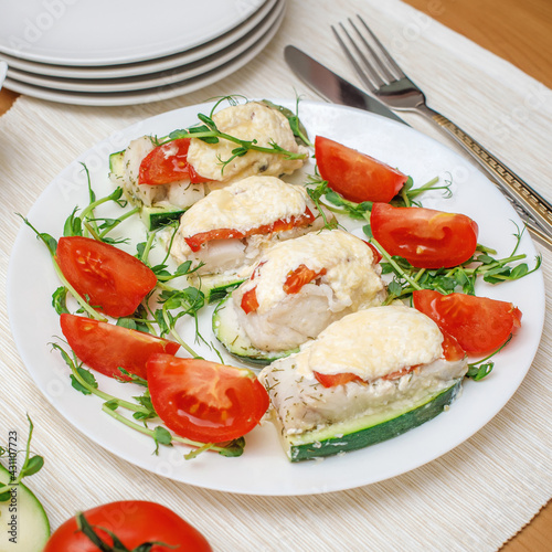 Baked fillet of codfish served with zucchini and tomatoes. Healthy food