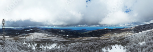 180 degree photo of the beech forest of the Nebrodi mountains in Sicily during a light snowfall in early spring. View of Etna. Monte Soro and the Aeolian Islands with the Tyrrhenian Sea. 