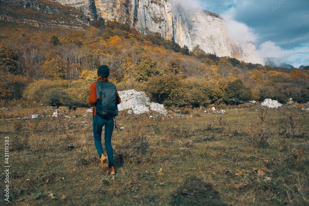 woman in jeans boots and a sweater with a backpack are resting in the autumn in the mountains in nature