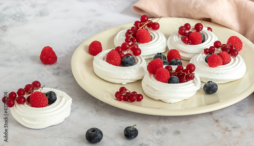 Fresh baking meringues or mini Pavlova on the plate. Sweet dessert decorated with different berries. 