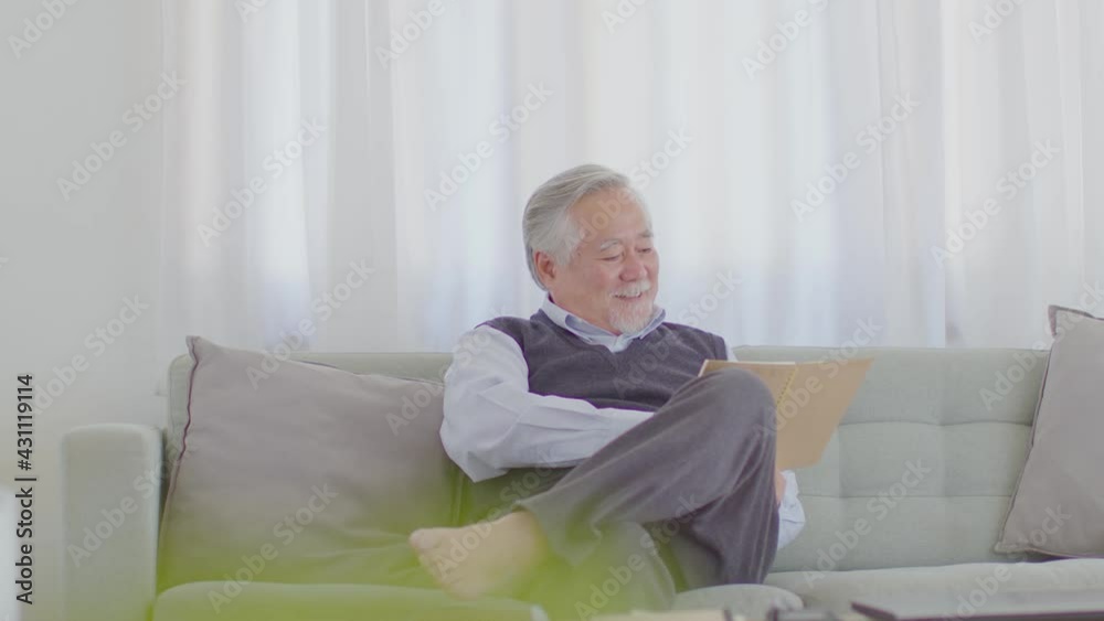 Calm of Happiness Asian Elderly man with white hairs sitting on sofa reading book enjoy relax and comfortable in cozy living room at home Calm of Happiness Asian Elderly man with white hairs sitting on sofa reading book enjoy relax and comfortable in cozy living room at home