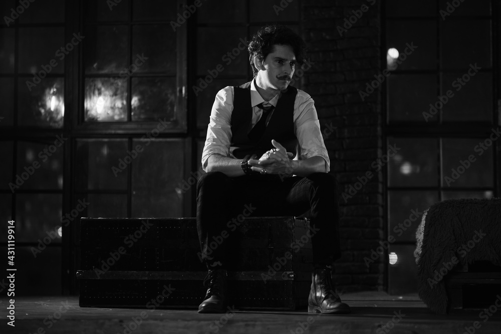 stylish dressed man stands at the window and looks into the distance. pensive man stands at night in a dark room. black and white photography stylish dressed man stands at the window and looks into the distance. pensive man stands at night in a dark room. black and white photography