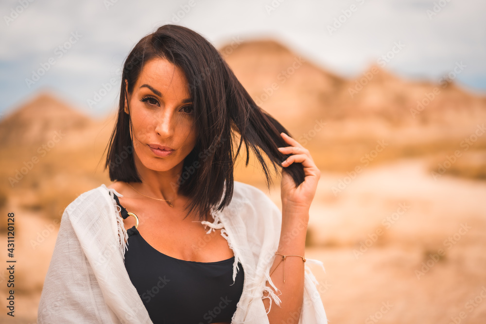 Sensual look of a young brunette Caucasian girl in a white dress sitting in a beautiful desert Sensual look of a young brunette Caucasian girl in a white dress sitting in a beautiful desert