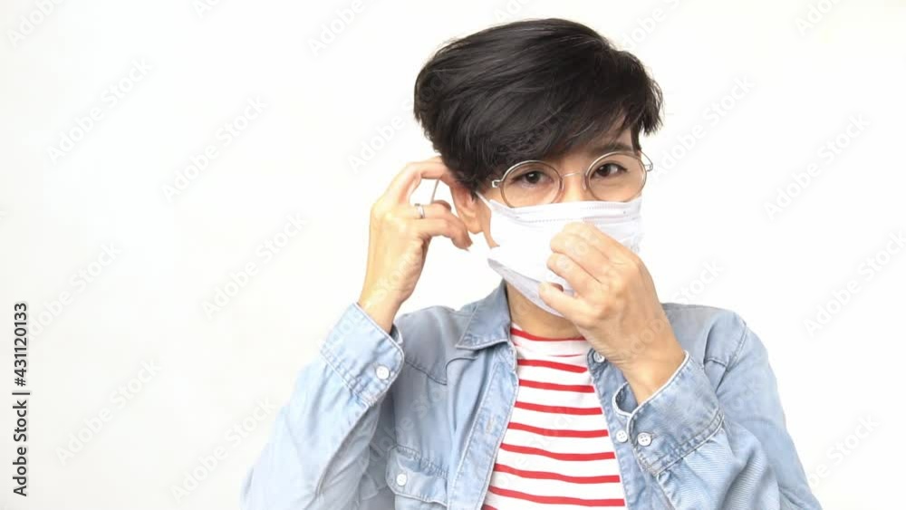 Studio portrait of stylish short hairstyle healthy Asian woman put on white medical medical face mask in slow motion. New normal for Covid-19 pandemic health care awareness. Studio portrait of stylish short hairstyle healthy Asian woman put on white medical medical face mask in slow motion. New normal for Covid-19 pandemic health care awareness.