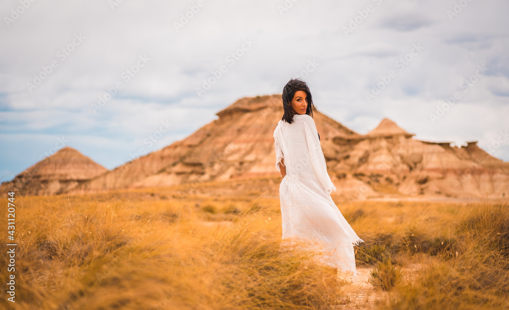 Fototapeta premium Young brunette Caucasian girl in a white dress and a black bikini enjoying in the beautiful desert
