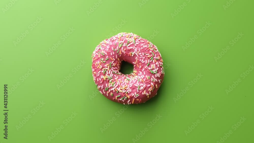 Fresh sweet doughnut covered by frosted pink chocolate bright sprinkle rotating isolated on green Fresh sweet doughnut covered by frosted pink chocolate bright sprinkle rotating isolated on green