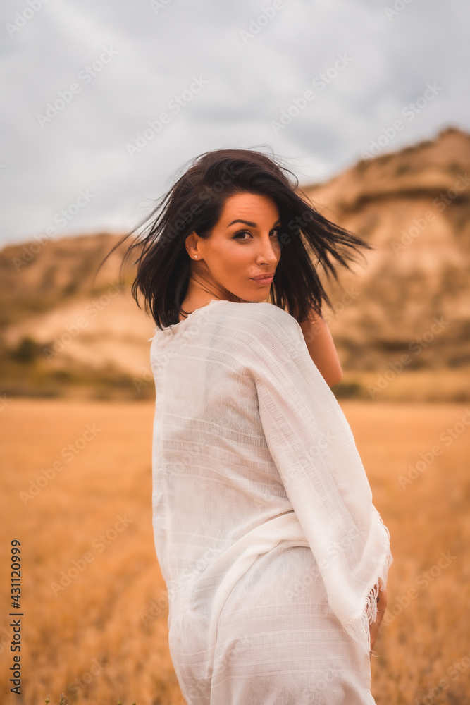 Fototapeta premium Portrait of a young brunette Caucasian model in a white dress and a black bikini enjoying in the beautiful desert one summer afternoon