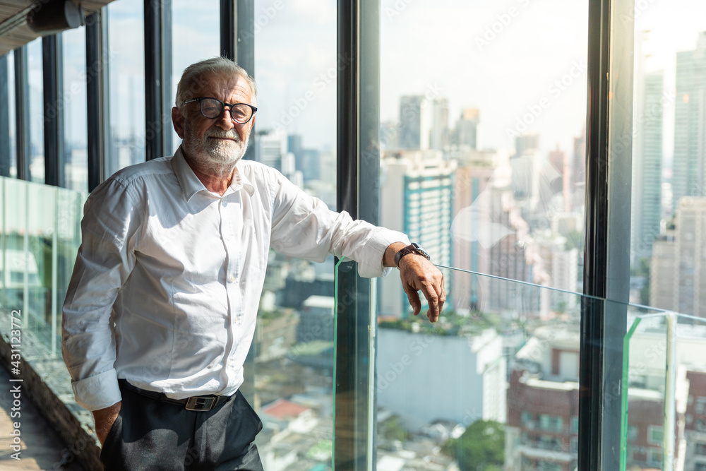 Old business man standing by the window. He is wearing glass , white shirt. He is in his 60th but look smart. The scene outside is cityscape. Old business man standing by the window. He is wearing glass , white shirt. He is in his 60th but look smart. The scene outside is cityscape.