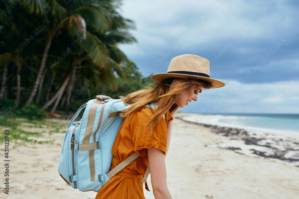 woman travels on the beach near the sea with a backpack on her back and tall trees in the background