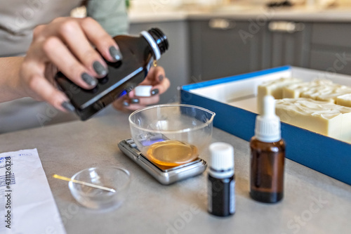 A soap-maker woman weighs aromatic oils for making cosmetics on a kitchen scale. Home spa. Small business