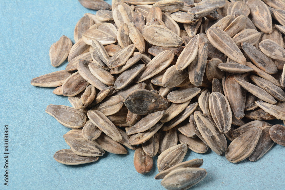 A pile of roasted sunflower seeds on blue background, copy space area for a text. Food beverage and wallpaper concepts A pile of roasted sunflower seeds on blue background, copy space area for a text. Food beverage and wallpaper concepts